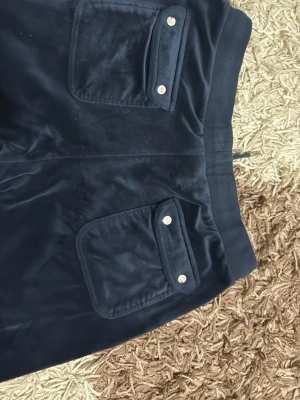 Mörkblå velour mjukisbyxor - Snygga mörkblå mjukisbyxor i mjuk velour med bred resår i midjan och två stora fickor bak med silverfärgade ärgade knappar. Perfekta för chill dagar och har en relaxed passform. Materialet är glansigt och känns lyxigt mot huden.