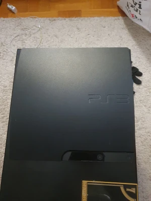 PlayStation 3 Slim svart konsol - Säljer en svart PlayStation 3 Slim från Sony. Konsolen har en matt finish och stilren design med rundade kanter. PS3-loggan är ingraverad på ovansidan och fronten har touchknappar för att starta och mata ut skivor. Perfekt för gaming och filmkvällar.