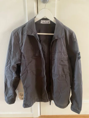 Grå overshirt från Stone Island - Snygg grå overshirt från Stone Island med klassisk patch på ärmen. Tillverkad i bomullstyg som känns lätt och bekvämt. Använd fåtal gånger. 