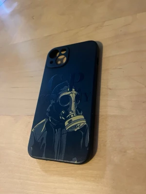 Svart mobilskal iphone 13 cp company - Coolt svart mobilskal med ett detaljerat motiv av en person i gasmask och jacka. Skalet har en matt finish och är tillverkat i plast, perfekt för dig som vill ha ett unikt och edgy tillbehör till mobilen. Iphone 13 cp company