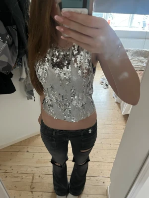 Silvrig paljettopp  - Säljer en croppad silvrig topp med paljetter och ribbad struktur. Toppen är ärmlös och har en snygg, figurnära passform som verkligen sticker ut. Perfekt för dig som vill glänsa lite extra och älskar detaljer som glittrar.
