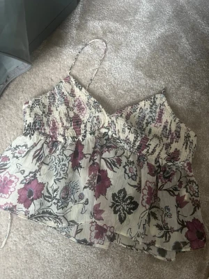 Blommig linnetopp från Zara XS - Eftertraktat Supersöt blommig linnetopp från Zara i krämvit med lila och svarta blommor. Smockad upptill, tunna axelband och luftig volang nedtill. Perfekt för varma dagar och ger en romantisk vibe till din outfit.