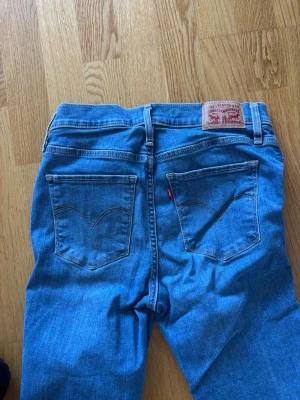 Blå Levi's skinny jeans - Säljer ett par klassiska blå skinny jeans från Levi's med den ikoniska röda lappen och läderpatch bak. Jeansen har två bakfickor med V-formad söm och är tillverkade i mjuk denim. Perfekta för en avslappnad och trendig look.