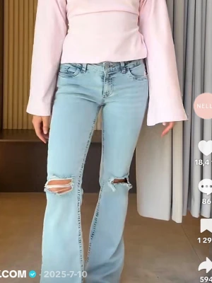 Ljusblå bootcut jeans med slitningar - Säljer ett par ljusblå bootcut jeans med slitningar vid knäna och rosa zigzag-detaljer på bakfickorna. Jeansen är mid-low waist och är rätt så stretchiga. Perfekta när du vill känna dig snygg men ändå var bekväm