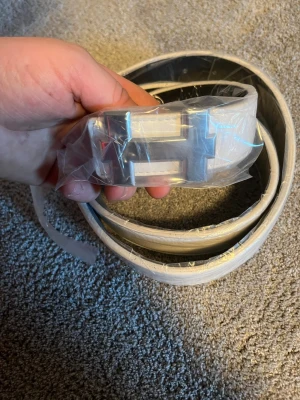 Vitt bälte med silverfärgat H-spänne - Snyggt vitt bälte med ett stort, silverfärgat H-format spänne. Bältet har en clean och modern look som passar till många olika outfits. Tillverkat i skinnimitation och har en stilren design som sticker ut. Ta helst insta box