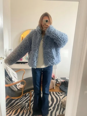 Ljusblå fluffig teddyjacka - Supermysig teddyjacka i ljusblått med oversized passform och hög krage. Jackan har en fluffig struktur och stängs med dragkedja framtill. Perfekt för att hålla värmen och ge en trendig look till din outfit.