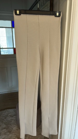 Beige ribbade leggings med slits - Säljer ett par beige ribbade leggings med slits framtill vid bensluten. De har hög midja och en tight passform som framhäver benen. Materialet är stretchigt och bekvämt 💕