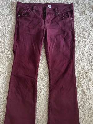 Vinröda bootcut jeans - Säljer ett par vinröda bootcut jeans med fem fickor och silverfärgade knappar. Jeansen har klassisk passform och är tillverkade i ett mjukt bomullsmaterial med lite stretch. Perfekta för dig som vill ha en snygg och bekväm look.