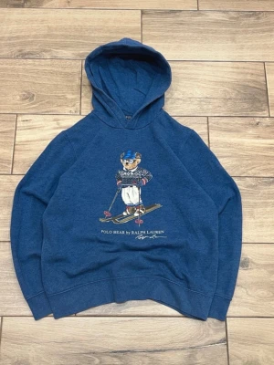 Ralph Lauren Polo Bear hoodie - Snygg marinblå hoodie från Ralph Lauren med klassiska Polo Bear-motivet (skidåkare). Storlek är 18–20 (barn), vilket motsvarar ungefär Herr S – passar perfekt som en mindre vuxenstorlek. 	•	Fint skick, sparsamt använd 	•	Mjuk och skön kvalitet 	•	Stilren och ikonisk design 	•	Inga synliga fläckar eller skador  Perfekt hoodie för både vardag och en mer uppklädd casual look.  Storlek: 18–20 (Herr S) Märke: Ralph Lauren Färg: Marinblå  Skickas snabbt 📦