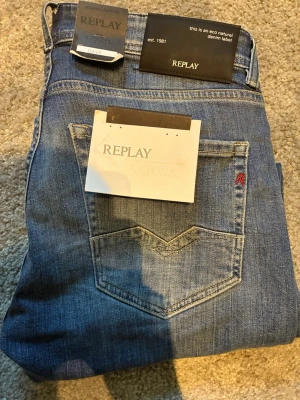Blå slim fit jeans från Replay - Snygga blå slim fit jeans från Replay med klassisk femficksdesign och subtila slitningar. Jeansen har en naturlig tvättad look och är tillverkade i ekologisk denim. Perfekta för dig som gillar en modern och avslappnad stil.