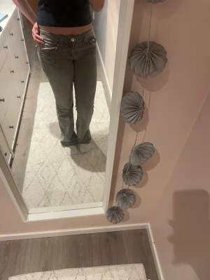 Grå bootcut jeans med låg midja - Säljer ett par gråa bootcut jeans med låg midja och klassisk femficksmodell. Jeansen har en avslappnad passform och stängs med dragkedja och knapp. Perfekta för en trendig och avslappnad stil.