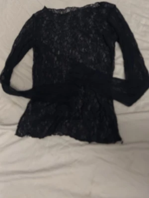 Svart spetsblus med lång ärm - Säljer en svart, långärmad blus i genombruten spets. Toppen har en rund halsringning och är helt täckt av ett elegant spetsmönster som ger en snygg och trendig look. Perfekt att styla lager på lager eller med ett linne under.