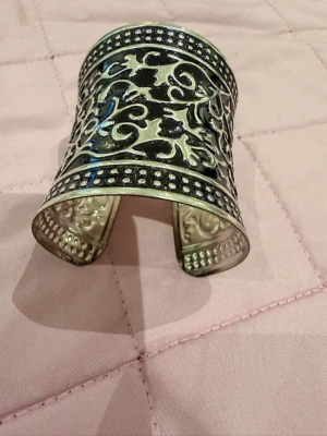 Brett silverfärgat manschettarmband - Snyggt brett manschettarmband i silverfärgad metall med detaljerade, utskurna mönster och prickiga kanter. Armbandet har en öppen design som gör det lätt att ta på och av. Perfekt för dig som vill sticka ut med accessoarerna.