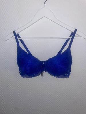 Blå spets-bh med bygel - Snygg blå bh med bygel och vadderade kupor. Bh:n har spetsdetaljer framtill och justerbara axelband för bästa passform. Perfekt för dig som vill ha något både bekvämt och stilrent under kläderna.