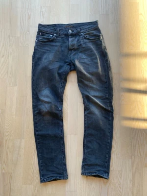 Nudie jeans - Svarta nudie jeans med klassisk femficksdesign och subtila slitningar på framsidan. Jeansen har raka ben och normal midja, perfekta för en avslappnad men ändå stilren look. Tillverkade i mjuk denim med stretch för extra komfort. Storlek 28/30, sitter mer som 29/31. Använda i ett par år, sparsamt.