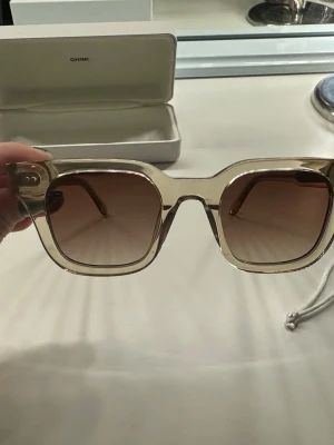 Beiga chimi solglasögon  - Snygga trendiga chimi solglasögon med transparent beige båge och fyrkantig form. Glasen är tonade i brunt och bågarna har en modern, chunky design. Modell 04. Man får me själva boxen samt påsen man lägger dom i! Original pris 1400kr och knappt använda💛