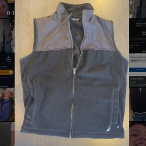 Svart fleeceväst med dragkedja - Säljer en svart fleeceväst med dragkedja och hög krage. Västen har en stilren design med en mörkare panel över axlarna och bröstet. Perfekt för lager-på-lager under kyligare dagar. Inga tecken på användning! Pris gå att diskutera vid snabb affär
