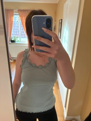 Ljusgrön ribbad linnetopp med spets - Supersöt ljusgrön ribbad linnetopp med spetsdetaljer runt ringningen och axelbanden. Toppen är figurnära och har vågig kant nertill. Perfekt att styla med jeans eller kjol för en chill look. Använt få gånger.  Fint skick.  Storlek: L  Material: 70% silke, 30% bomull. Nypris: 350-450. 