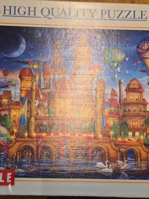 6000bitars pussel - Säljer ett stort pussel med motivet 'Downtown' av Ciro Marchetti. Pusslet mäter 169 x 119 cm och har ett färgstarkt, fantasifullt stadsmotiv med slott, luftballonger och svanar. Perfekt för dig som gillar utmanande och detaljerade pussel. Kan inte lova att alla bitar finns, därav priset