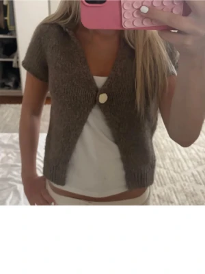Kort brun stickad Zara kofta - Kortärmad brun stickad kofta med en stor vit knapp framtill. Koftan har en djup v-ringning och super mjukt🥹❤️ HELT SLUTSÅLD