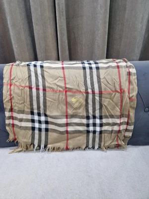 Beige rutig sjal  - Snygg beige sjal med klassiskt rutmönster i svart, vitt och rött. Sjalen har fransar i kanterna och ett guldfärgat broderi. Perfekt accessoar för att lyfta din outfit.