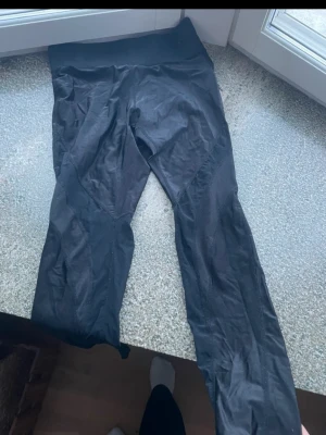 Svarta sportleggings med hög midja - Säljer ett par svarta träningstights med hög midja. De är tillverkade i ett stretchigt och följsamt material som passar perfekt för gymmet eller löpning. Tightsen har en stilren design utan synliga loggor och sitter tajt längs benen. Använts en del och är därför i använt skick.
