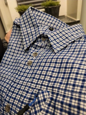Blårutig kortärmad skjorta S - Snygg kortärmad skjorta med blått och vitt rutmönster. Klassisk krage, knappar framtill och en bröstficka. Perfekt för en avslappnad stil. Tillverkad i mjuk bomull som känns skön mot huden.