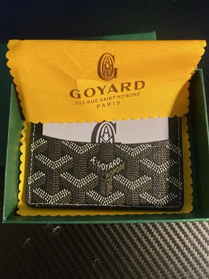 Svart kortfodral  - Snyggt svart kortfodral med det klassiska vita och gråa mönstret. Fodralet har flera kortfack och är tillverkat i canvas med läderdetaljer. Perfekt för dig som vill ha en stilren och exklusiv accessoar i fickan.