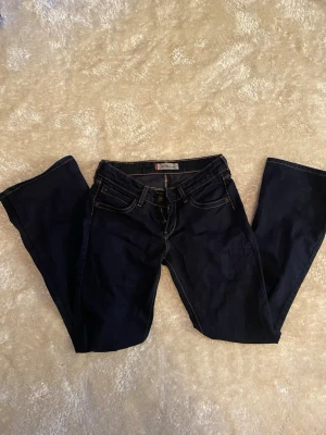 Levi's 572 Bootcut jeans mörkblå - Säljer ett par mörkblå Levi's 572 Bootcut jeans med klassiska kontrastsömmar och fem fickor. Jeansen har bootcut-passform och den ikoniska röda Levi's-lappen på bakfickan. Midjan rakt över: 34cm. Innerben: 76cm