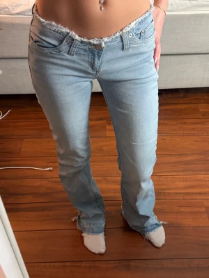 No waist jeans Nelly - Säljer ett par ljusblå bootcut jeans med rå, fransig kant i midjan och vid bensluten. Är tillverkade i denim med stretch. Perfekta för en avslappnad och trendig look.