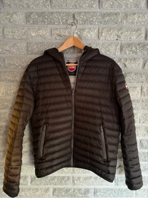 Svart dunjacka med huva från Colmar - Säljer en svart dunjacka från Colmar med huva och dragkedja framtill. Jackan har två sidofickor med dragkedja och quiltad design. Perfekt för kalla dagar och riktigt snygg till streetwear-stilen. Storlek 50.