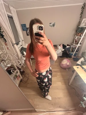 Orange kortärmad t-shirt - Mysig pyjamas med en korallfärgad t-shirt och svarta byxor med gulligt Hello Kitty-mönster. T-shirten är kortärmad och byxorna har resår i midjan för extra komfort. Perfekt för chillkvällar hemma.