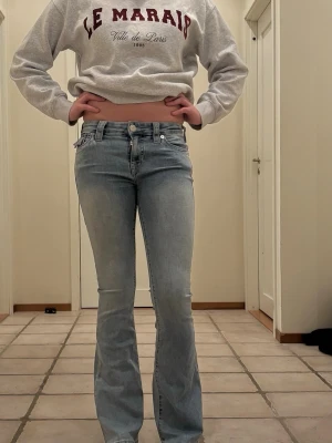 Ljusblå bootcut jeans från True Religion - Säljer ett par ljusblå bootcut jeans från True Religion med klassiska kontrastsömmar och snygga fickdetaljer bak. Jeansen har låg midja och är tillverkade i mjuk denim med stretch för skön passform. Perfekta för en avslappnad och trendig look.