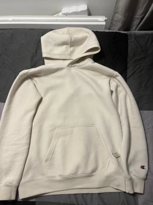 Beige hoodie från Champion - Säljer en stilren vit hoodie från Champion i storlek 162-167. Hoodien har en klassisk huva, stor magficka och det ikoniska Champion-logotypen broderad på ärmen. Tillverkad i mjukt och bekvämt material som passar perfekt till en avslappnad look.