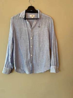 Randig blåvit skjorta från Hampton republic - Klassisk blåvit randig skjorta från Hampton republic med lång ärm och knappar framtill. Tillverkad i tunn och luftig bomull, perfekt för en avslappnad men ändå stilren look. Liten broderad logga på bröstet och snygg krage. Riktigt skön skjorta till sommarn.