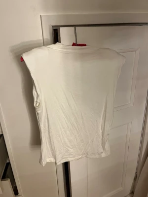 Vit ärmlös topp - En enkel vit ärmlös topp i mjukt tyg. Passar perfekt till jeans eller kjol för en clean och avslappnad look. Materialet känns lätt och skönt mot huden. Puffiga axlar.