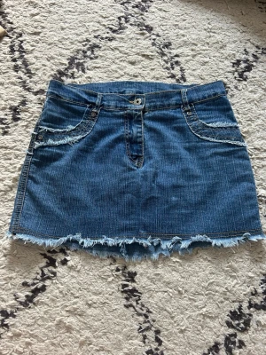 Blå jeanskjol med fransad kant - Snygg blå jeanskjol i kort modell med fransad nederkant och detaljer. Perfekt för en avslappnad och trendig look. Skriv om du har frågor, jag är även öppen för prisförslag!🥰