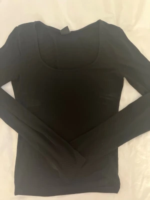 Svart långärmad topp Gina Tricot 💞 - En svart långärmad topp från Gina Tricot med rundad, djup urringning. Toppen har en slim passform och är tillverkad i mjukt stretchigt material, perfekt att styla med jeans eller kjol. 💞