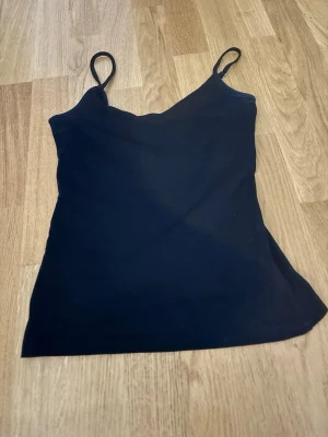 Svart enkel linnetopp - Säljer en svart linnetopp med smala axelband som är justerbara och rak passform. Toppen är stilren och passar perfekt till jeans eller kjol. Materialet känns mjukt och stretchigt, troligen bomull eller en bomullsblandning. Perfekt basplagg för sommaren!