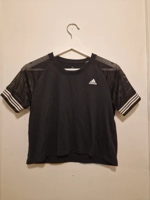Svart mesh t-shirt från Adidas - Croppad modell med Adidas-logga på bröstet. Perfekt för träning eller en aktiv vardag. Inköpt I Spanien och använd 2 gånger på semestern.