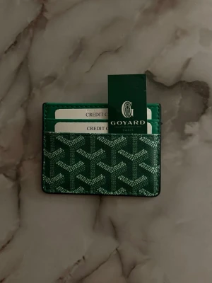 Grön kortfodral  - Snyggt grönt kortfodral  med det klassiska mönstret i vitt och svart. Fodralet har flera fack för kort och är tillverkat i tåligt canvasmaterial med exklusiv känsla. Perfekt för dig som vill ha en stilren och lyxig accessoar i fickan.