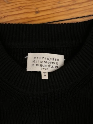 Svart stickad tröja Maison Margiela - Säljer en svart stickad tröja från Maison Margiela. Tröjan har rund halsringning, ribbstickad struktur och långa ärmar. Perfekt för dig som gillar minimalistisk och stilren design. Märkeslappen med de ikoniska siffrorna sitter i nacken.