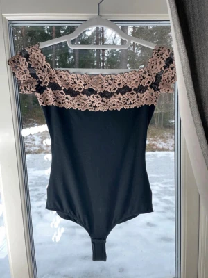 body från intimismi  med spetsdetaljer  - intimissimi body som inte säljs längre. Har slutat säljas i butik. Storlek S. Snygg body med breda axelband och off shoulder-design. Överdelen har vackra spetsdetaljer i beige med blommönster som ger en romantisk touch. Materialet ser stretchigt och mjukt ut, perfekt för att skapa en feminin siluett. 