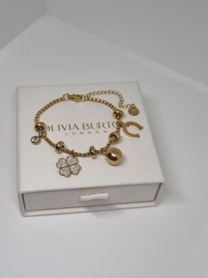 Guldigt charmarmband  18k guldpläterad  - Snyggt guldigt armband frånmed flera olika berlocker, bland annat en fyrklöver med gnistrande stenar, en hästsko, en rund boll och små pärlor. Armbandet har en tunn kedja och klassisk karbinhake. Perfekt accessoar för att lyfta din stil. Lådan ingår ej.