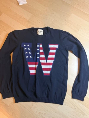 Mörkblå tröja Skill Denim USA-flagga - Mörkblå tröja från Skill Denim med stor W på bröstet i amerikanska flaggans färger och mönster. Rund halsringning, långa ärmar och ribbade muddar. Perfekt för dig som gillar statement-plagg och coola detaljer.