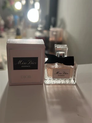Miss Dior Essence parfym 5 ml - Söt och elegant parfym från Dior, Miss Dior Essence, i en liten glasflaska på 5 ml. Flaskan är rektangulär med en svart rosett runt halsen och har en genomskinlig design. Kommer i en ljusrosa kartong med klassisk Dior-logga. Perfekt att ha med i väskan.