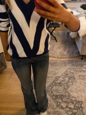 Blåvit stickad tröja med V-ringning - Säljer en stickad tröja med breda blå och vita ränder i ett coolt zigzag-mönster. Tröjan har djup V-ringning och långa ärmar. Perfekt för dig som gillar en avslappnad men ändå trendig stil.