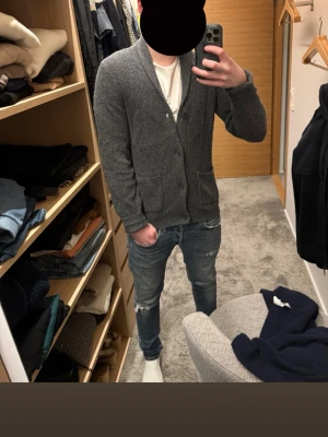 Cardigan tröja - Mysig mörkgrå kofta med sjalkrage och knäppning framtill. Två stora fickor framtill. Perfekt att slänga på sig över en t-shirt för en avslappnad look.