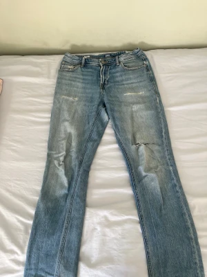 Ljusblå raka jeans från Jack & Jones - Säljer ett par ljusblå jeans från Jack & Jones med raka ben och slitna detaljer på låret och knät. Klassisk femficksmodell med knappgylf och cool vintagekänsla. Perfekta för dig som gillar en avslappnad och trendig stil.