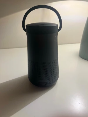 Bose bärbar högtalare svart - Snygg och stilren bärbar högtalare från Bose i svart färg. Cylindrisk form med praktiskt handtag upptill och perforerat metallgaller nedtill för bra ljudspridning. Perfekt för att ta med sig musiken överallt man får mer laddare.